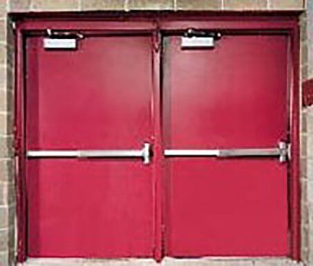 Two red double doors with horizontal push bars and overhead closers