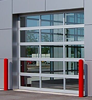 Glass roll-up garage door with white framing and red bollards in front of a building.