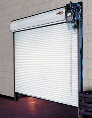 White roll-up garage door partially open in a tiled building interior with exposed mechanism on the right.