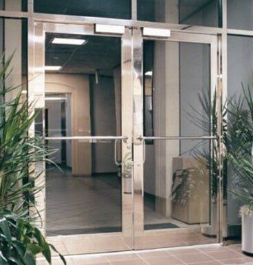 Glass office entrance with double doors, potted plants, and a hallway beyond