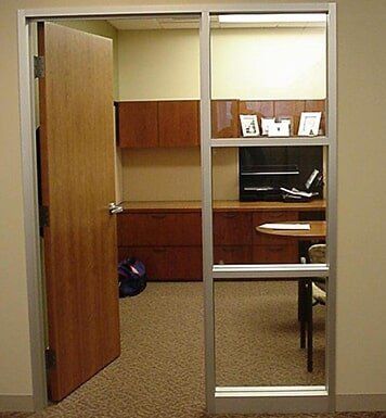 Open office doorway with wood cabinets, desk, and framed photos behind a glass partition