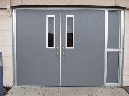 Gray double doors with narrow windows, set in a light-colored building wall