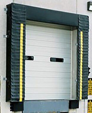 Closed gray industrial loading dock door with yellow side bumpers and black trim