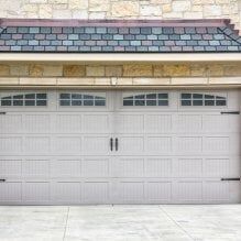 White two-car garage door with small windows and black handles beneath stone siding