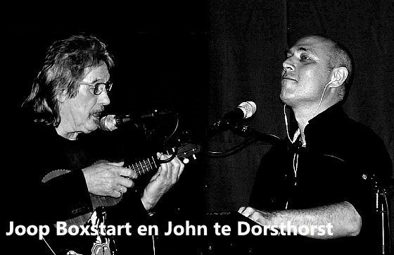 Two men performing music. One plays an instrument and sings; the other sings. Both have microphones. Black and white.