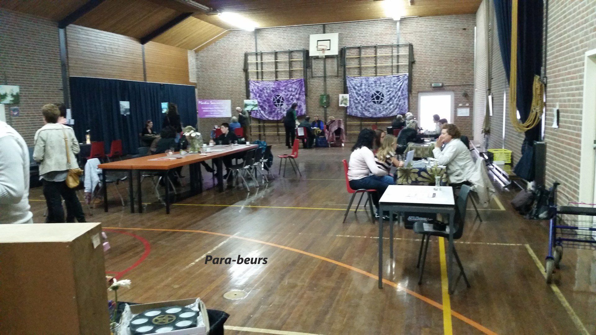 A school gymnasium with tables set up for an event, people milling about.