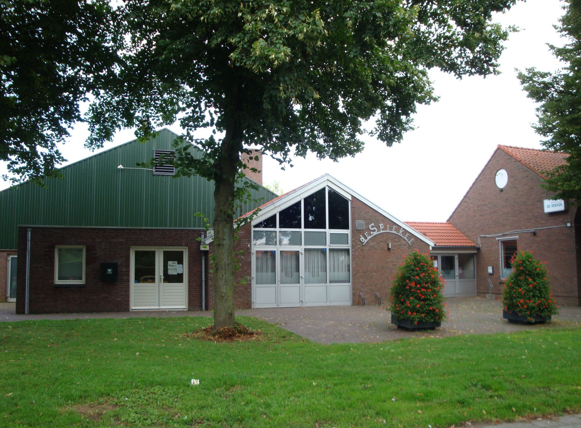 Buildings with green and red roofs, brick walls, and a tree in front, on a grassy lawn.