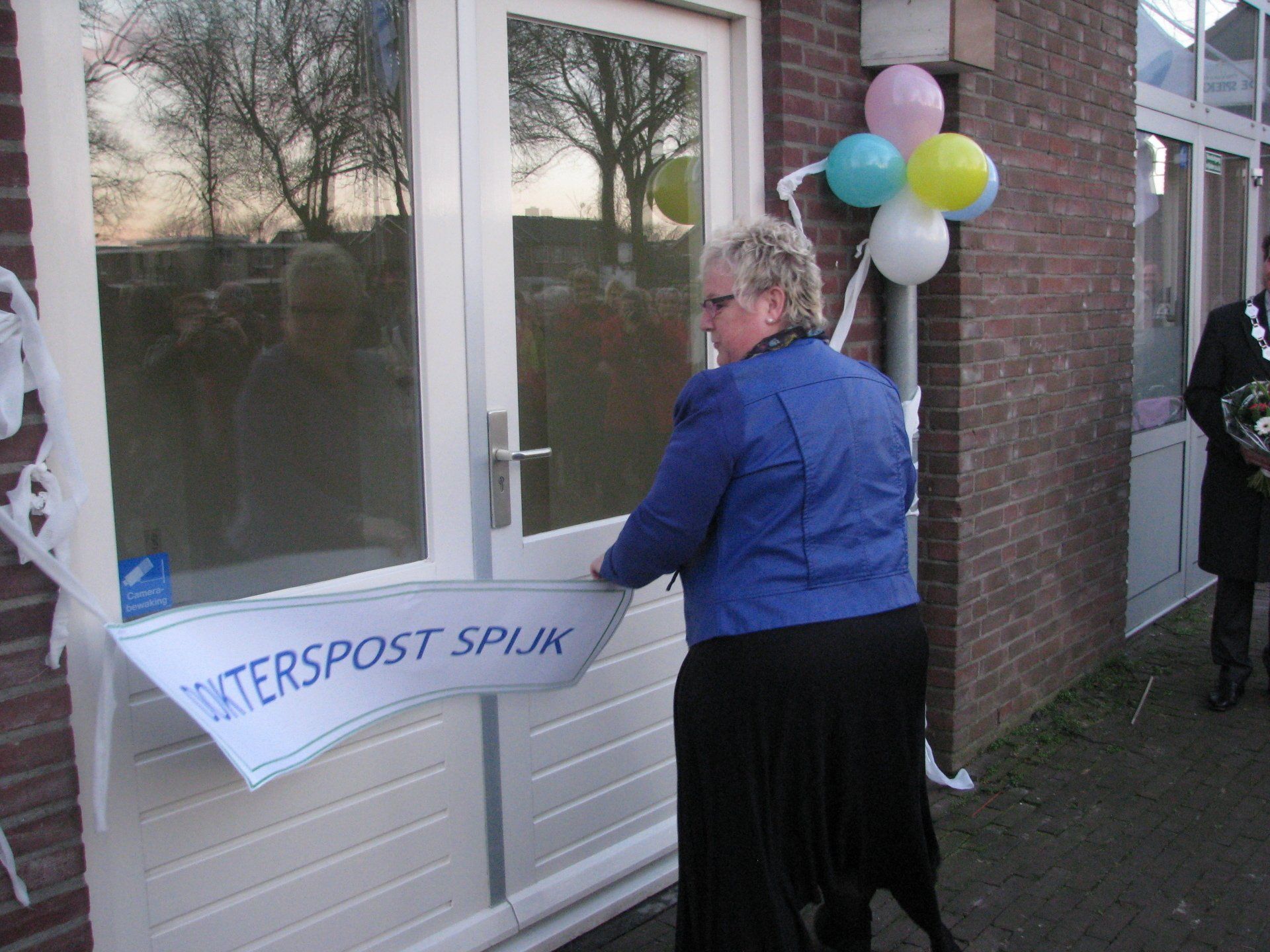 Woman cutting a ribbon at a building entrance. Sign reads 