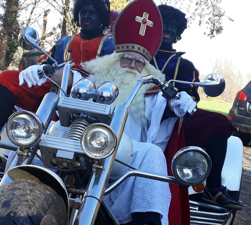 Sinterklaas on a motorcycle with two Zwarte Pieten. They are in a sunny outdoor setting.