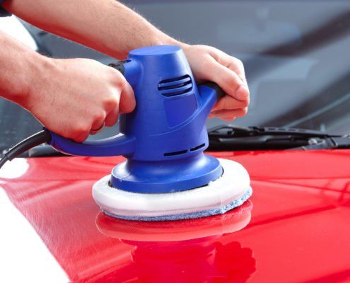 Eine Person poliert ein rotes Auto mit einer blauen Maschine