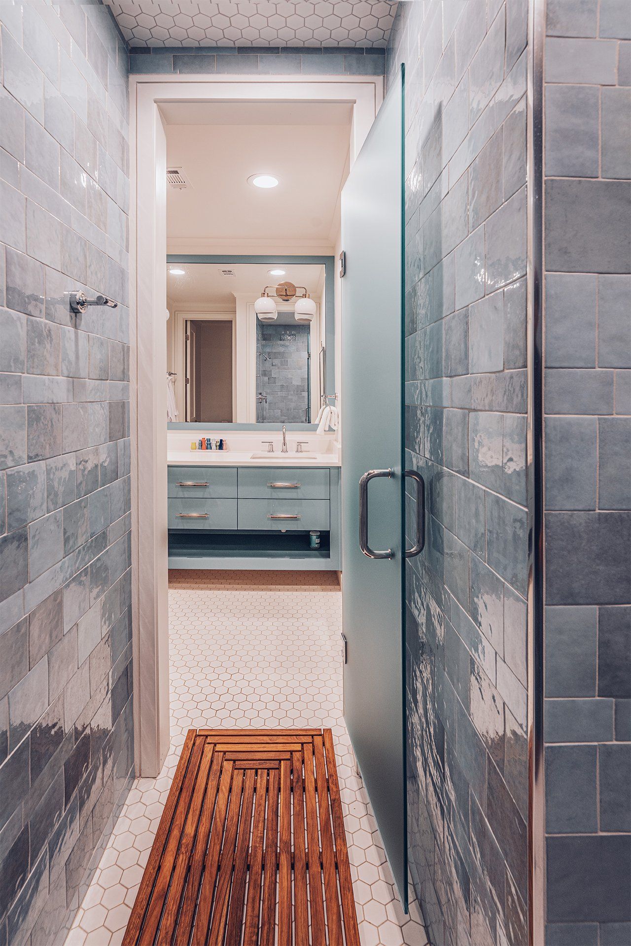 A bathroom with a walk in shower and a wooden mat on the floor.
