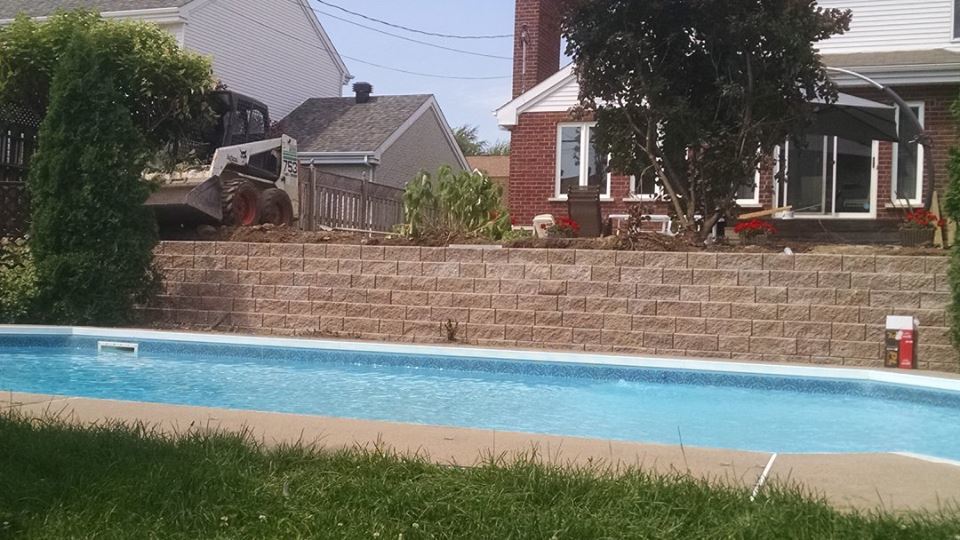 backyard with green grass and above ground pool and brick wall