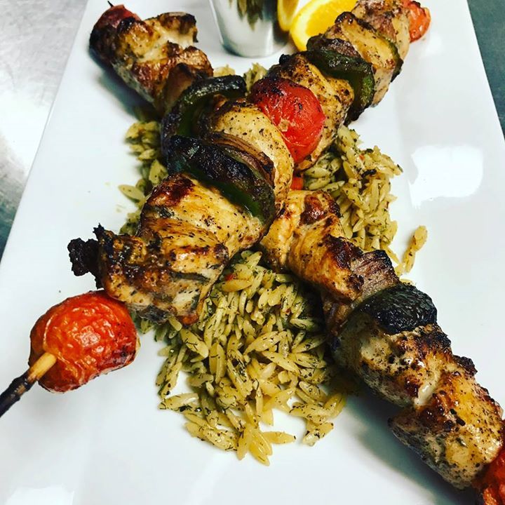 A white plate topped with chicken skewers and rice