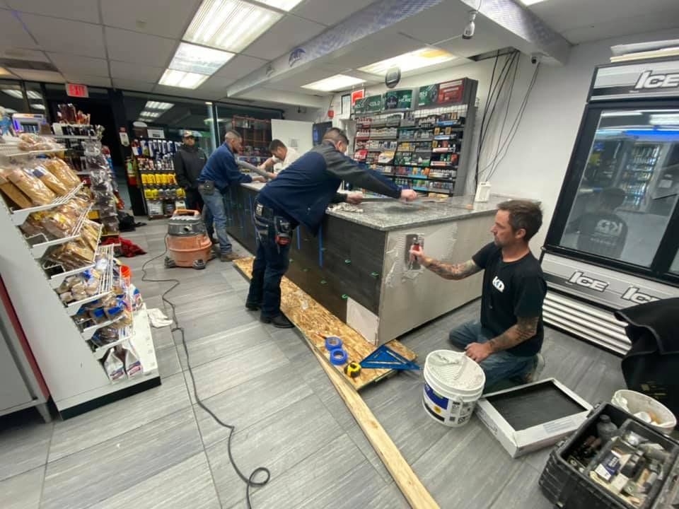 Workers installing tiles on a counter in a store. Tools and supplies are visible on the floor.