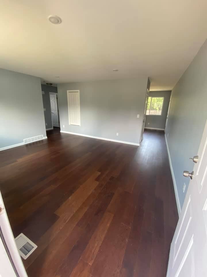 Empty room with dark wood floors, light blue walls, and a white door.
