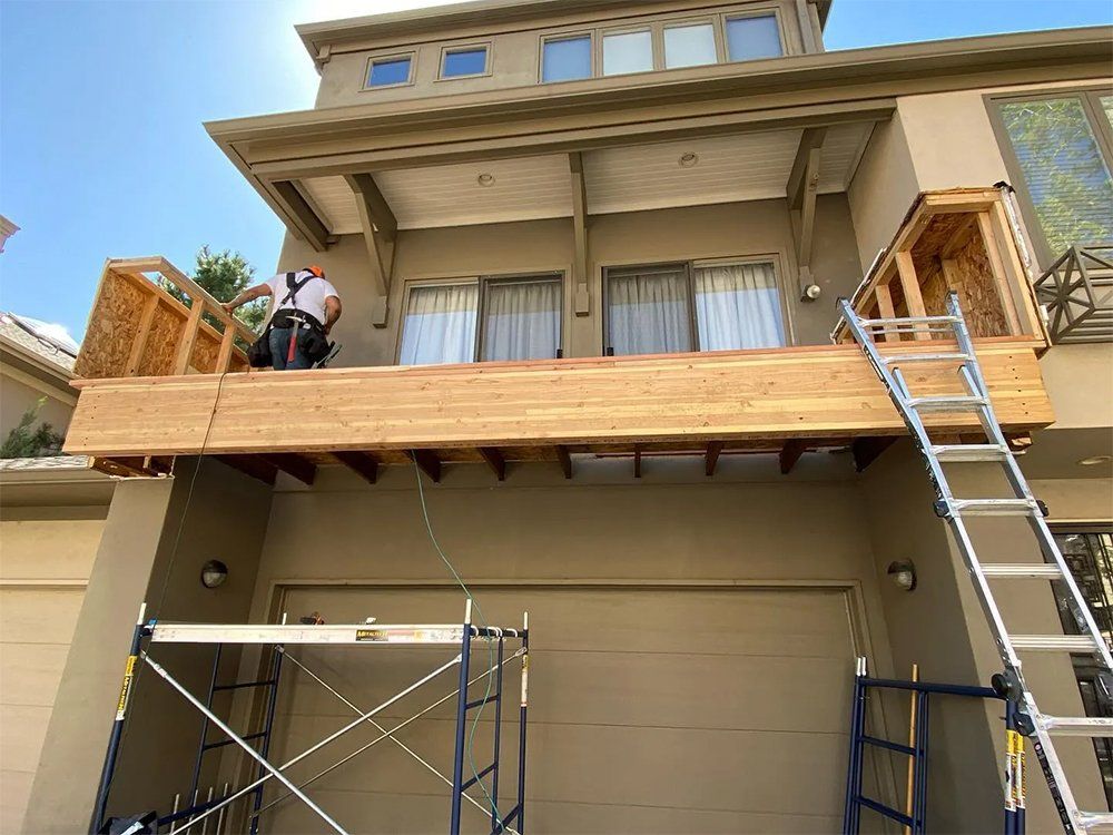 A worker builds a wooden deck above a garage. Scaffolding, ladder, house. Sunny day.