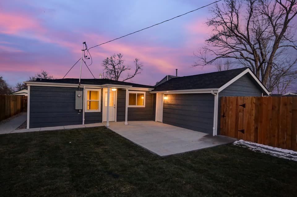 A blue house with attached garage, concrete patio, and fenced yard at dusk.