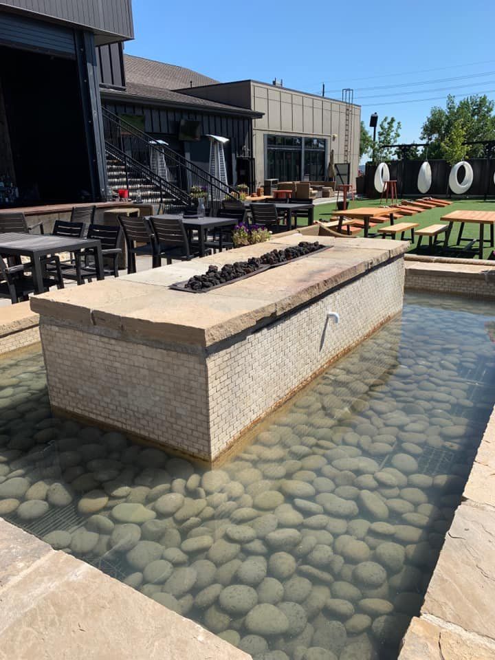 Outdoor patio with water feature and fire pit; tables and chairs; sunny day.