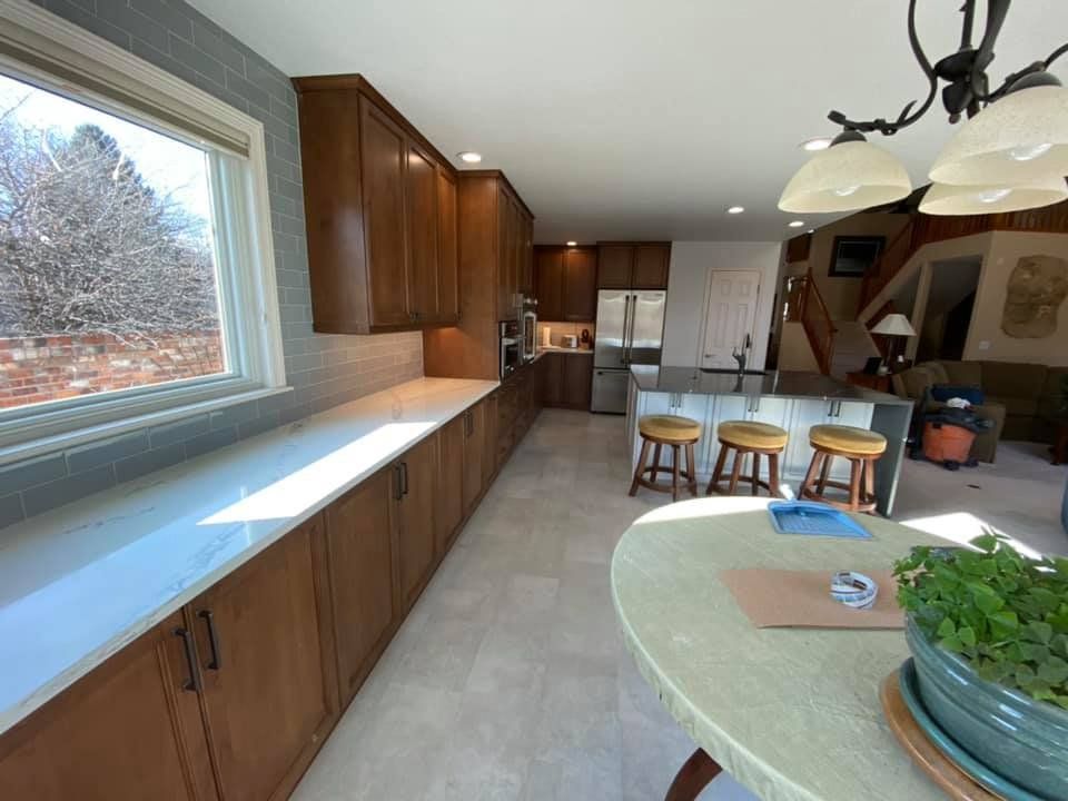 Spacious kitchen with wood cabinets, white countertops, and a central island. A round table with a plant is in the foreground.