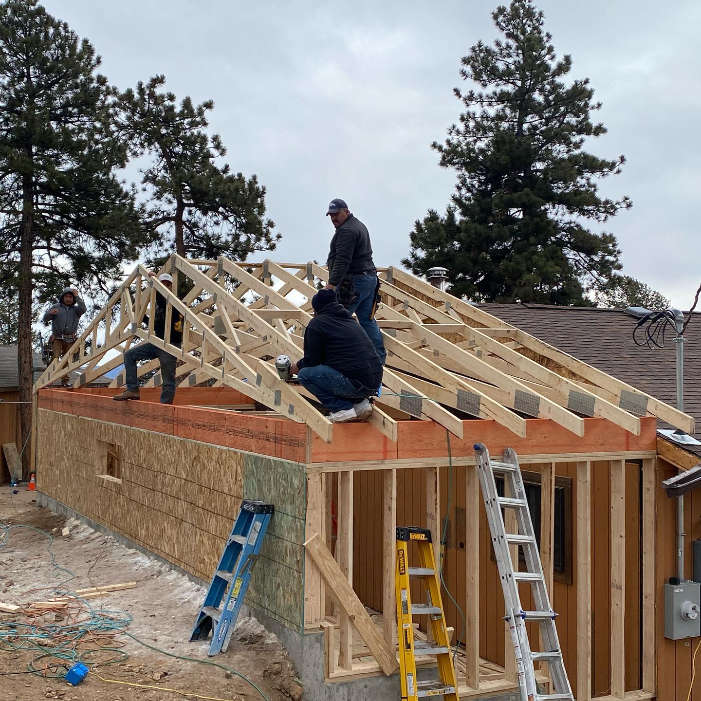 Workers framing a house roof with wooden trusses on a brick building under construction