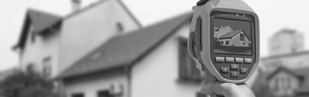 Auf ein Haus gerichtete Wärmebildkamera, die ein Wärmebild auf dem Bildschirm anzeigt.
