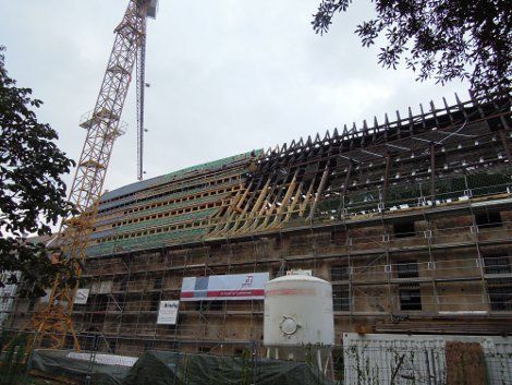 Gebäude im Bau mit einem Kran, freiliegenden Dachbalken, Gerüst und einem weißen Wassertank.