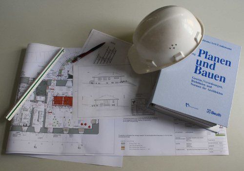 Baupläne, ein weißer Bauhelm, ein Stift und ein Buch mit dem Titel „Planen und Bauen“.