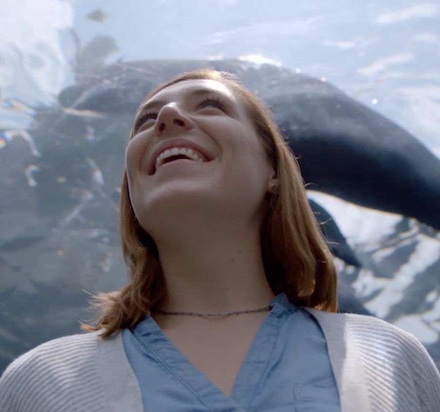 A woman in a blue shirt is smiling in front of a whale
