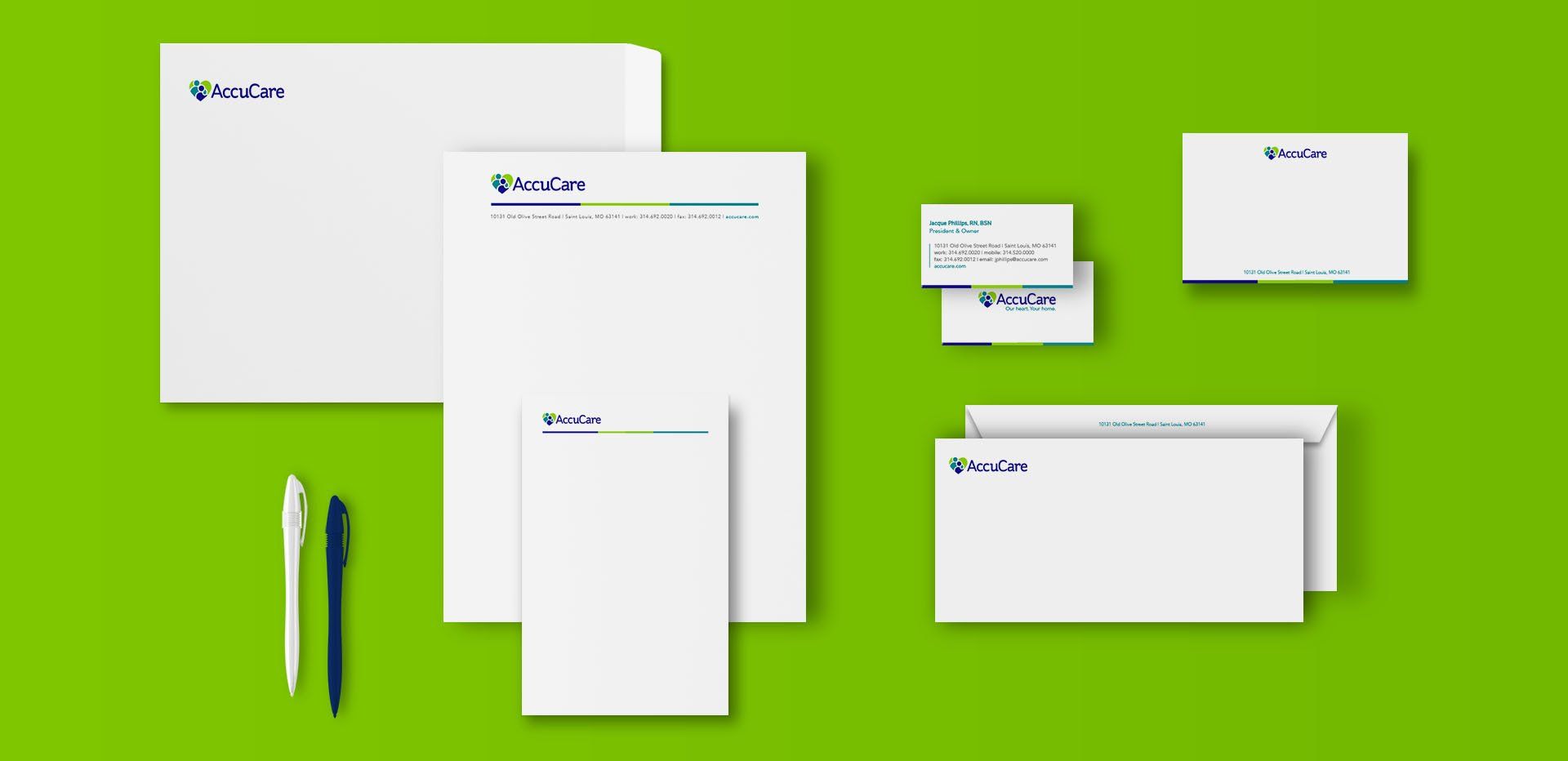 A set of business cards , envelopes , and a pen on a green surface.