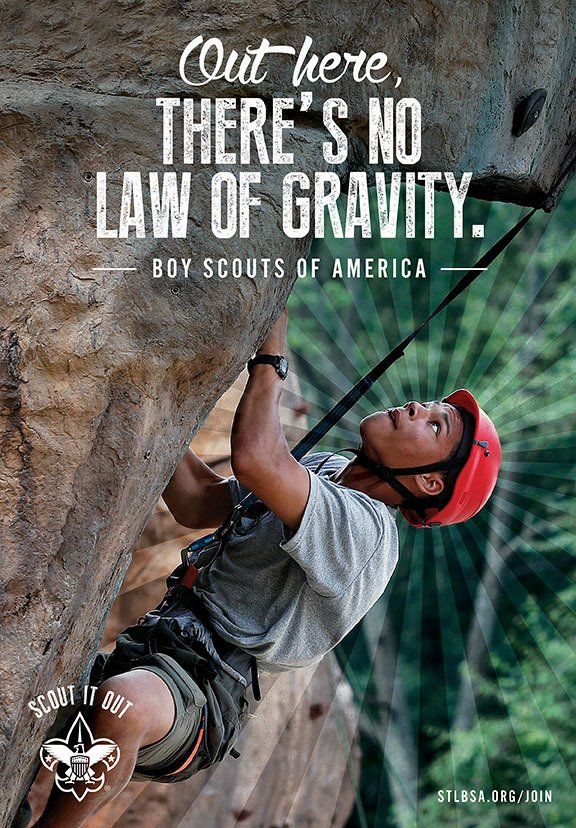 A boy scout is climbing a rock wall.