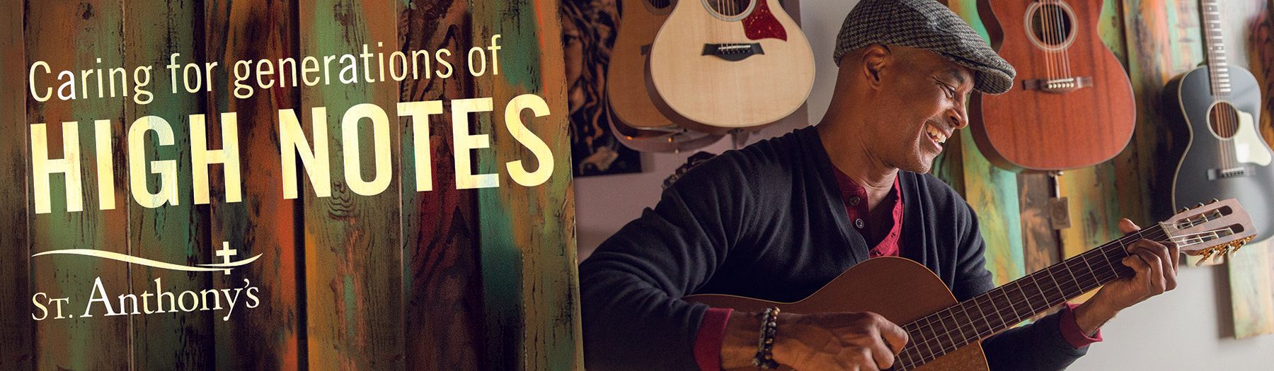 A man is playing a guitar in front of a wall of guitars.