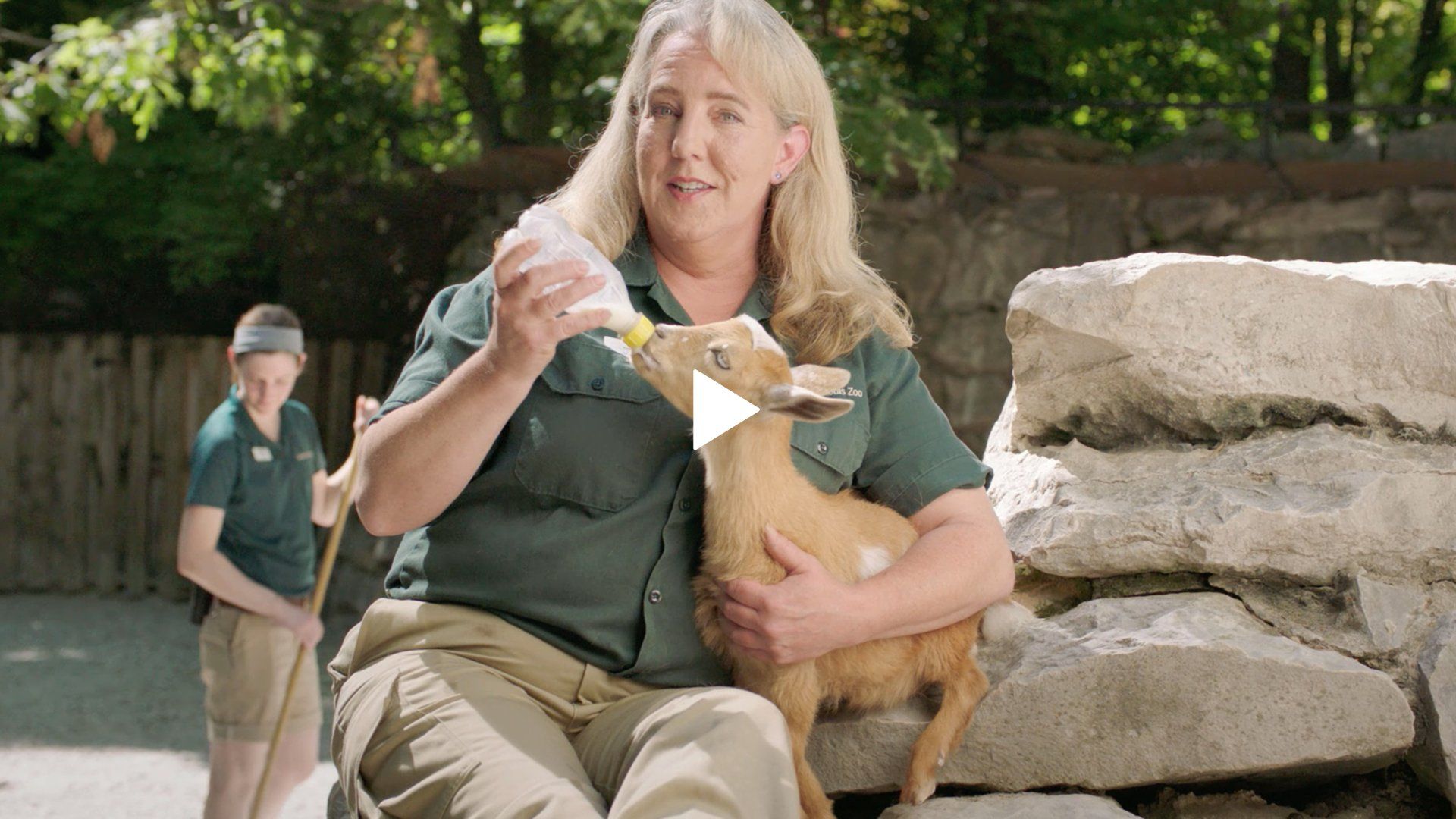 A woman is feeding a baby deer from a bottle.