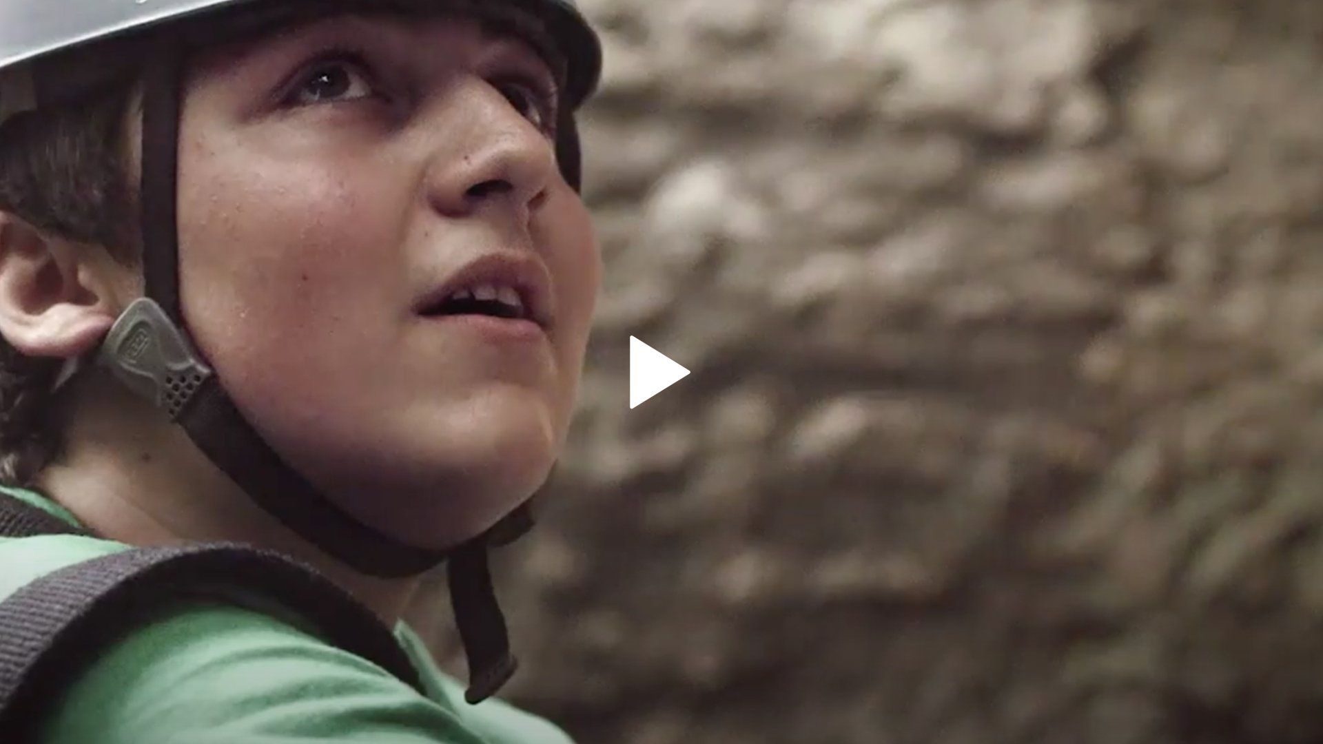 A young boy wearing a helmet and a green shirt is looking up.