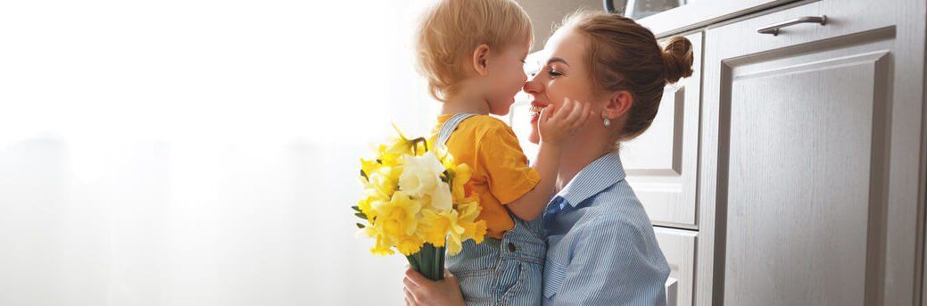 A little boy is holding a bouquet of flowers and kissing his mother on the cheek.