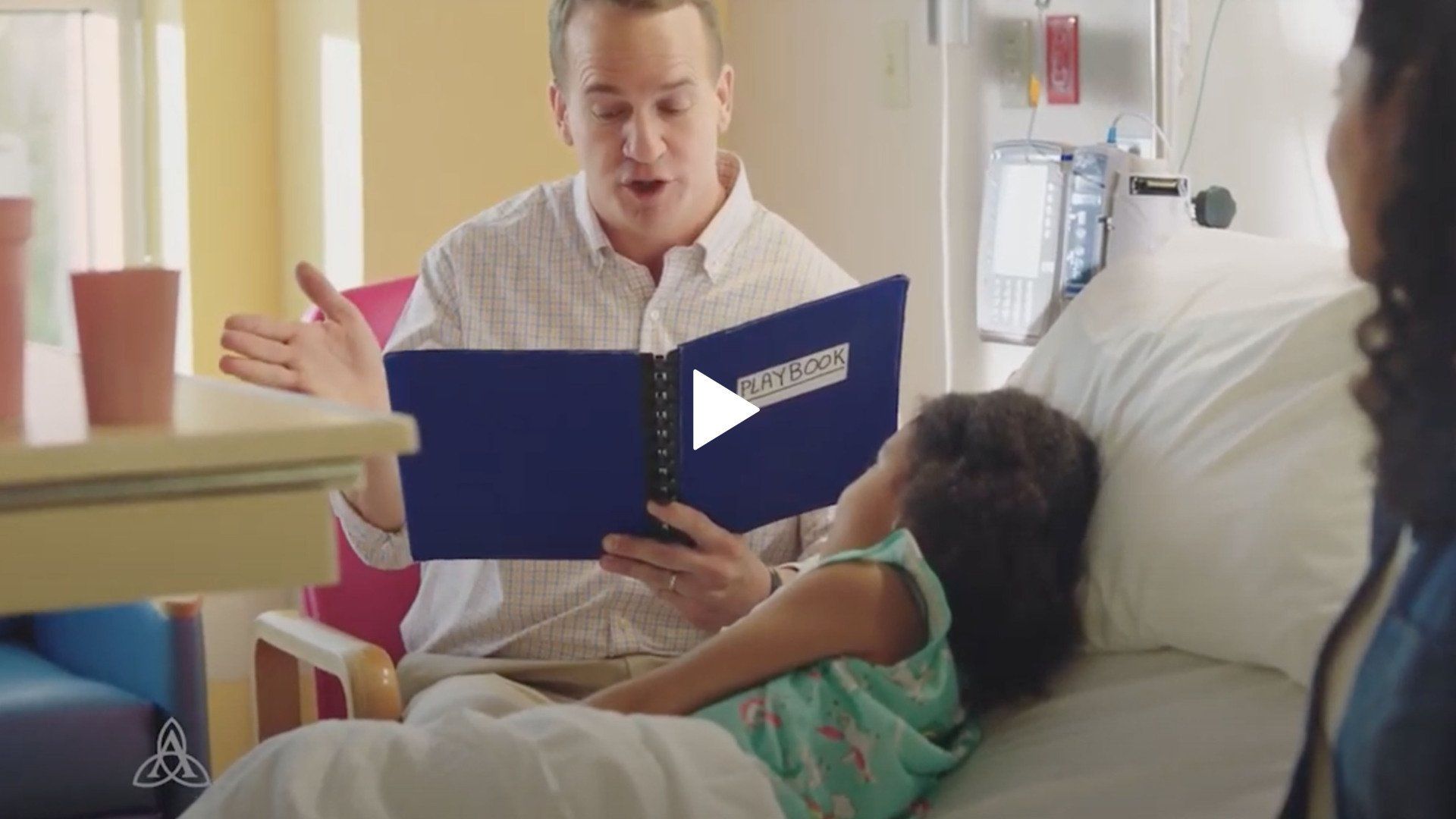 Peyton Manning is reading a play book to a little girl in a hospital bed.