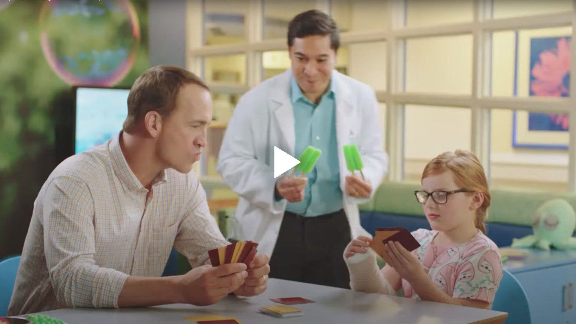 Peyton Manning and a little girl are sitting at a table playing cards.