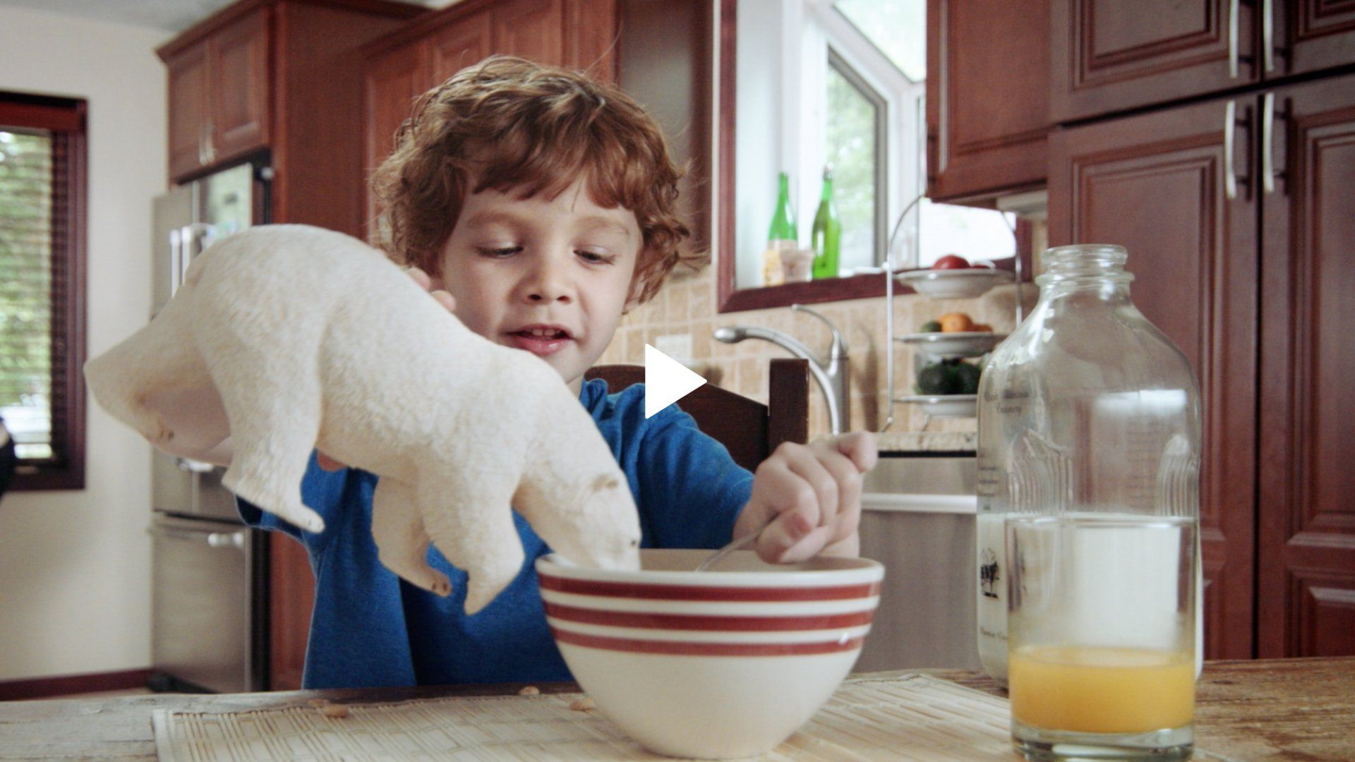 A young boy is playing with a stuffed polar bear in a bowl of cereal.