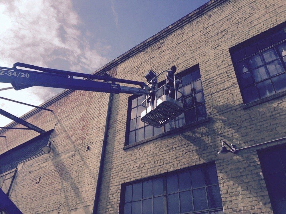 A man in a bucket is cleaning a window on a brick building.
