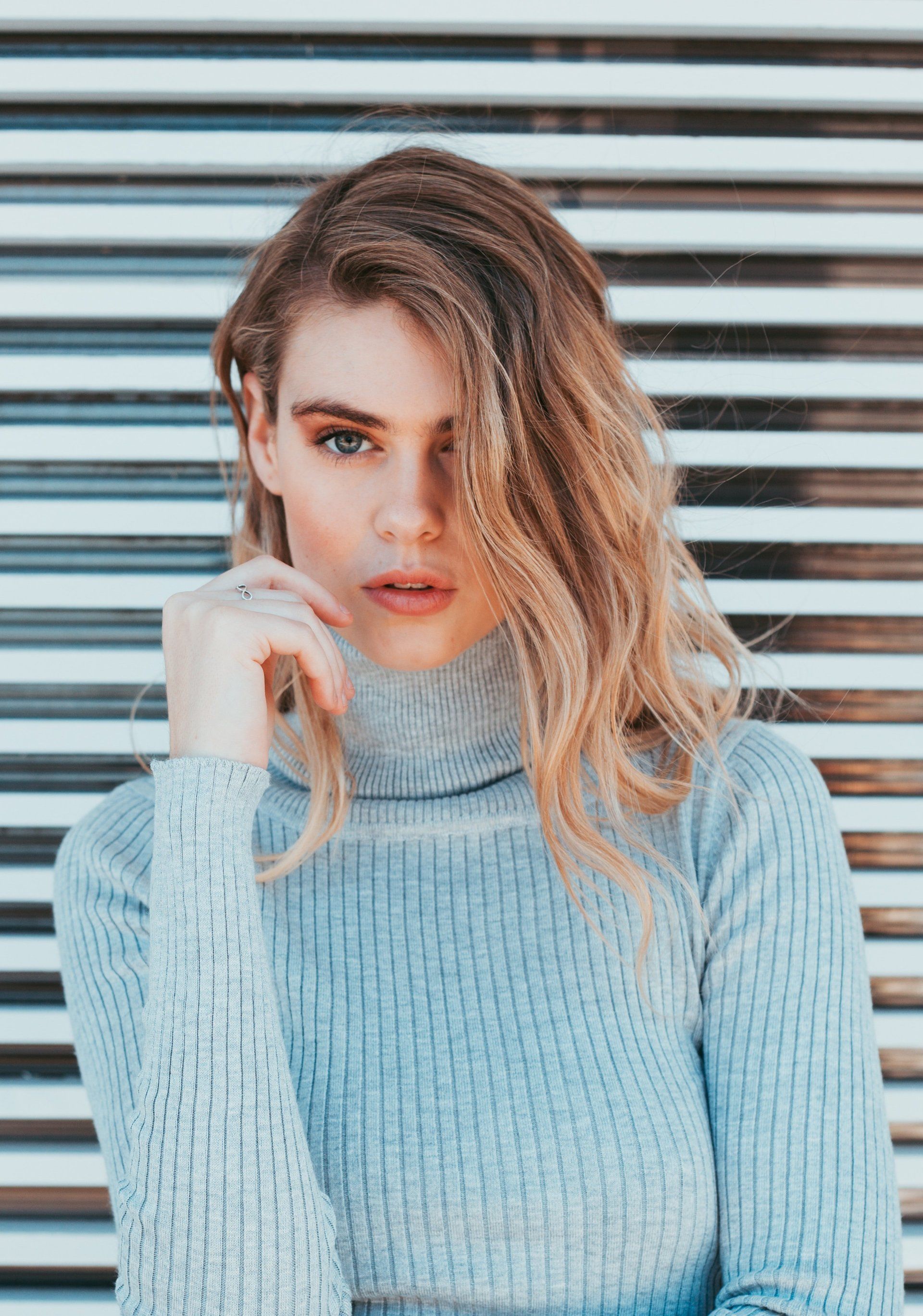 Une femme en pull bleu se tient devant un mur rayé.