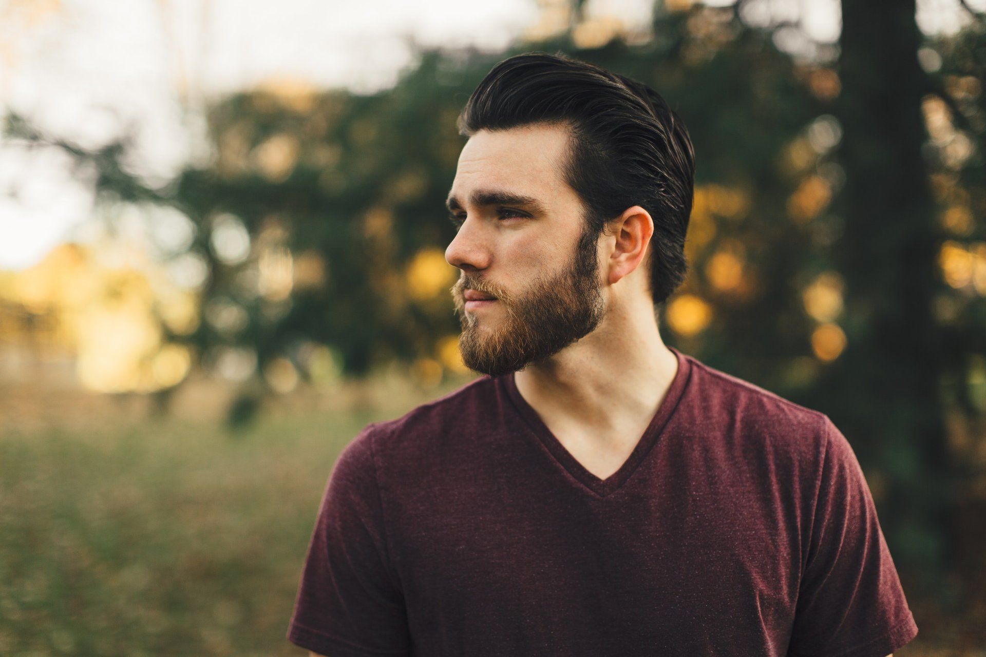 Un homme avec une barbe porte un t-shirt marron et se tient debout dans un champ.