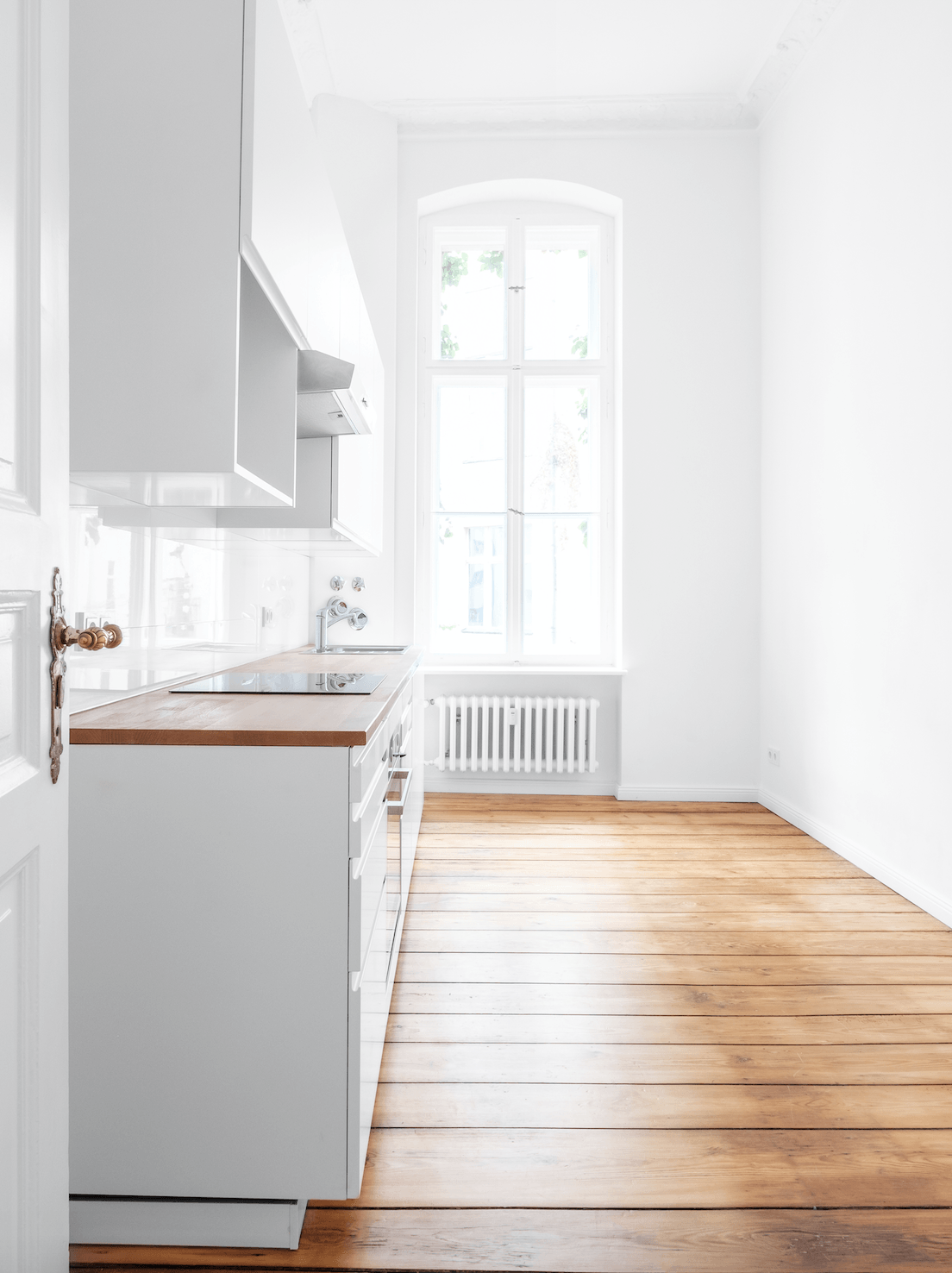 An empty kitchen with white cabinets and wooden floors.