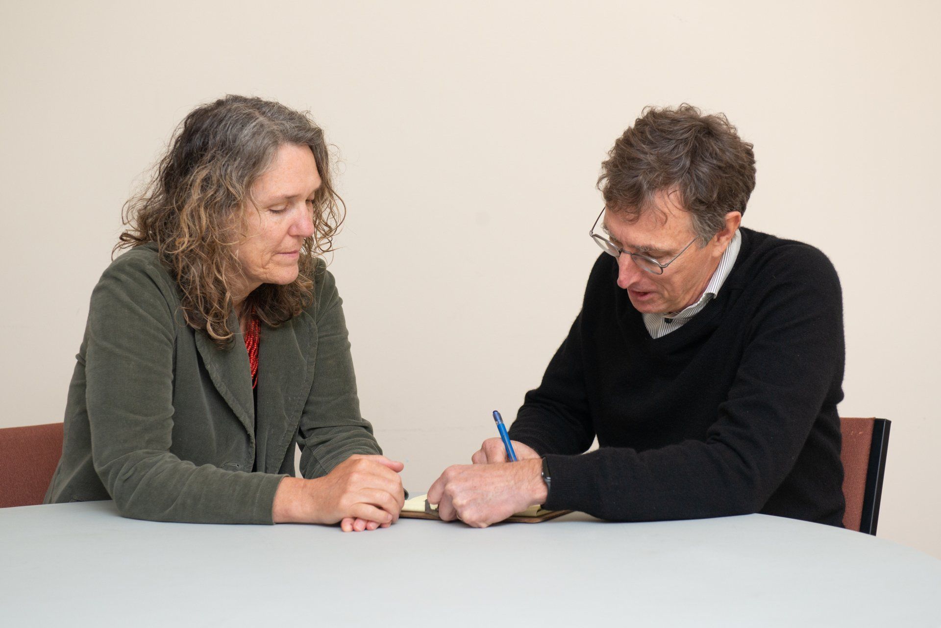 Greg Hessel and a client are seated at a table, looking down as one writes with a blue pen