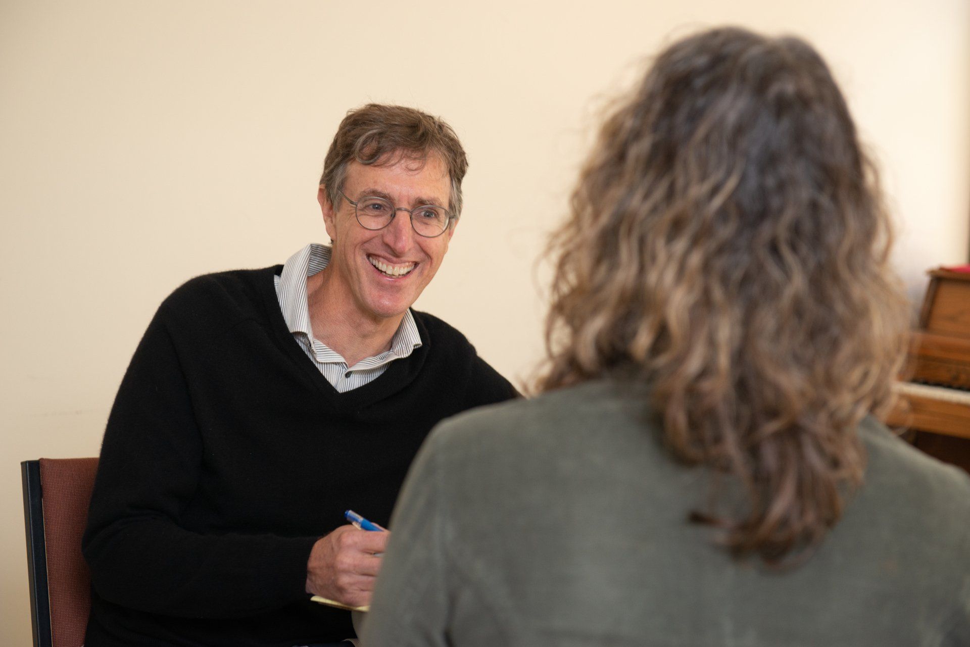 Greg Hessel is talking across a table, one smiling and taking notes in a bright office.