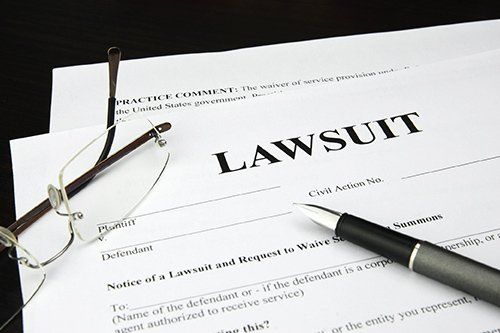 Lawsuit paperwork with a pen and eyeglasses on a dark surface.