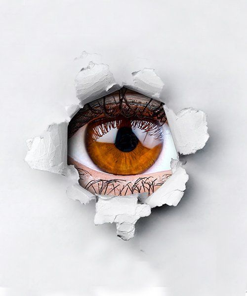 Brown eye peeking through a torn white paper.