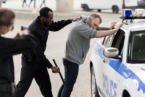 Police officers arresting a person by a police car; one officer holds a baton.