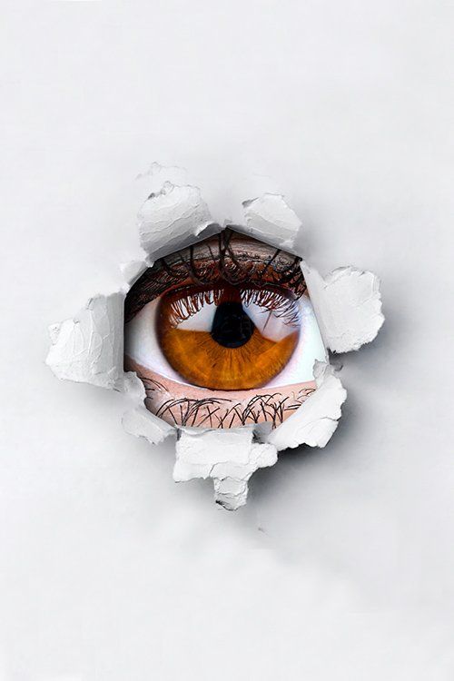 Brown eye peers through a torn white paper hole.