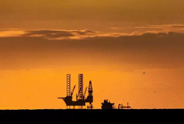 Uma plataforma de petróleo é silhuetada contra um céu de pôr do sol.