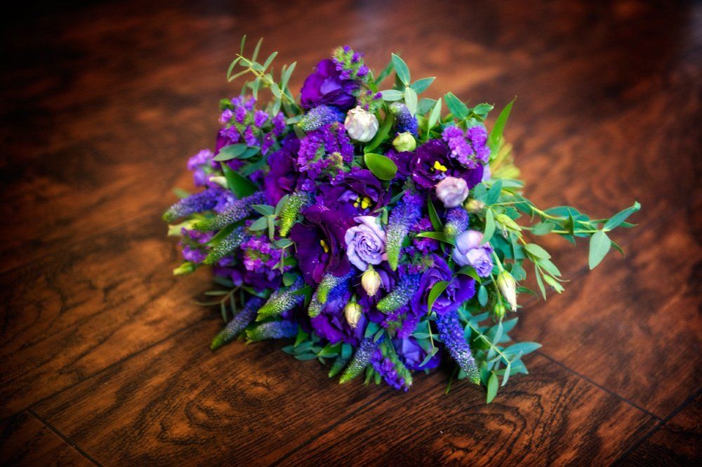 Bouquet of dark purple flowers and greenery on a dark wood surface.