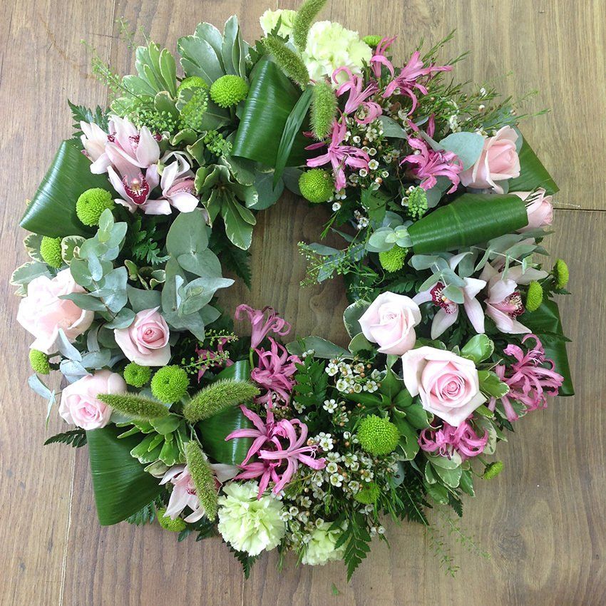 Floral wreath with pink roses, green foliage, and pink accents on wood surface.